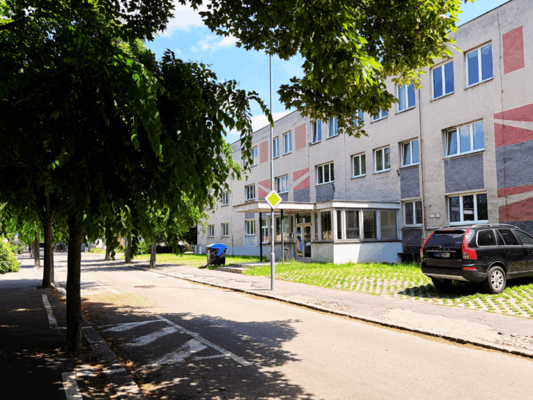 Budova Pozemných stavieb Trenčín s kancelárskymi priestormi, vstupom do objektu a stromovou alejou pri ceste.